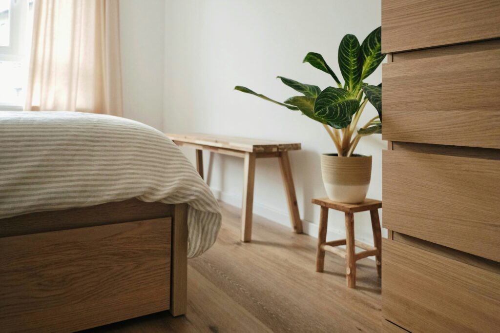 Modern bedroom decor ideas - the photo shows a bedroom with the end of a bed showing, a bench sitting on the far end, a small stool holds a plant pot, and beside it, is a wooden wardrobe.